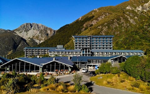 Multi-storey hotel complex with low-pitched roofs set against steep bush-covered mountain slopes
