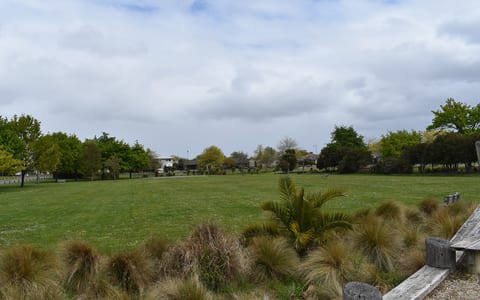 Open grassed reserve with trees and plantings under cloudy sky