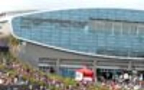 Large arena building with crowd on surrounding lawn at outdoor event