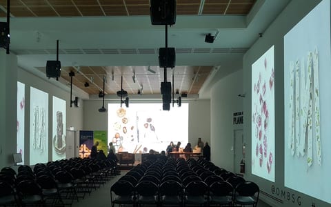 Large gallery space configured with rows of chairs facing a presentation screen