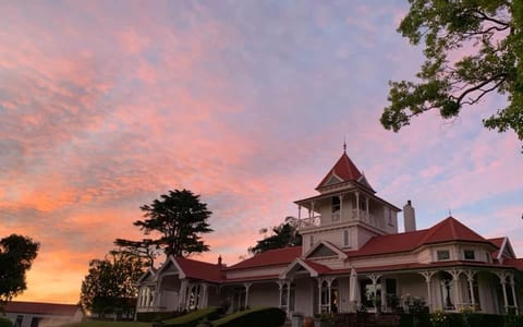 Victorian-era homestead with red-tiled roof and wraparound veranda at sunset
