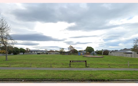 Open grass reserve with a playground area and signage near a residential street