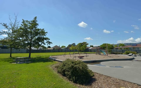 Open grassed reserve with playground equipment, picnic table and trees