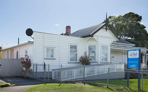 White timber villa exterior with pitched roof and decorative gable, white picket fence, green lawn