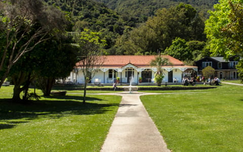 White homestead building on lawn with hills and trees behind