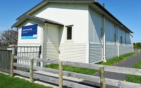 White-painted corrugated metal hall with a low-pitched roof and signage beside a path