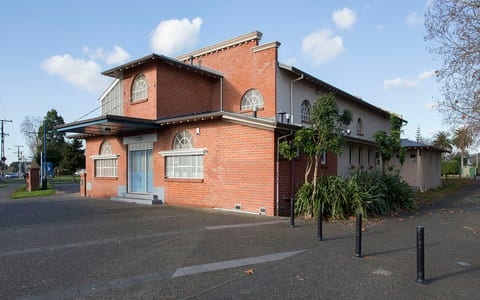 Red-brick two-storey community hall exterior with arched windows, car park and street frontage