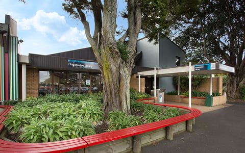 Library building exterior with large tree, curved bench seating and planting