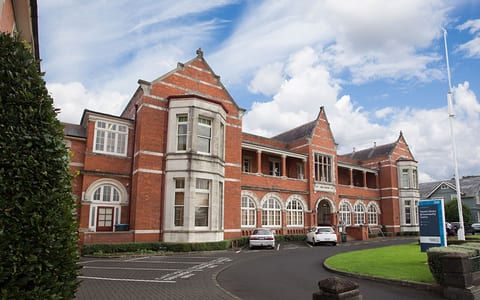 Two-storey red brick heritage building with gabled roofline, arched windows and circular drive
