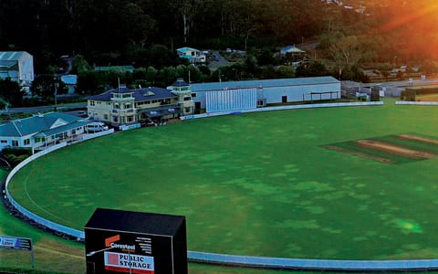 Cricket oval at dusk with a scoreboard in the foreground and surrounding hills