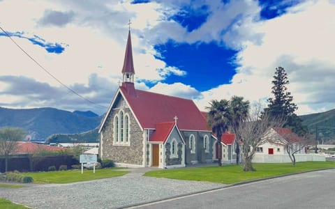 Stone church with red corrugated roof and steeple against blue sky