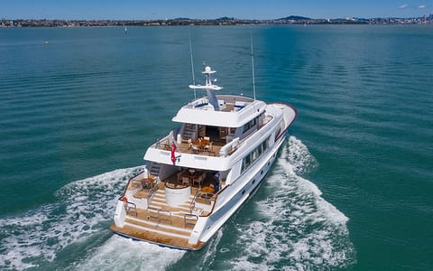 Large motor yacht underway in harbour with city skyline in background