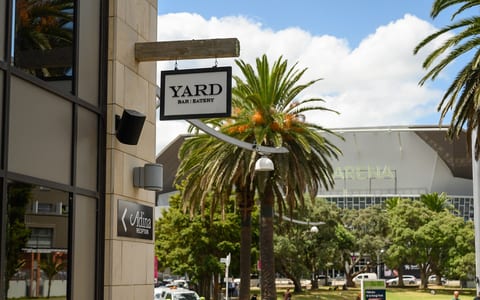 Stone-clad building exterior with hanging signage, trees and arena beyond