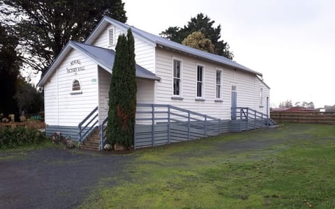 White weatherboard hall exterior with blue-grey ramp and stairs, lawns and trees