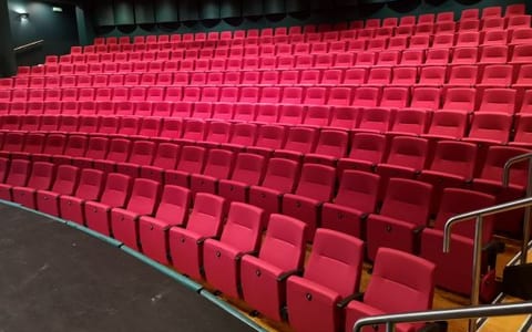Theatre auditorium with tiered rows of red upholstered seats