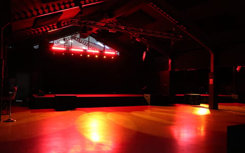 Dark warehouse interior with red stage lighting, exposed truss and open concrete floor