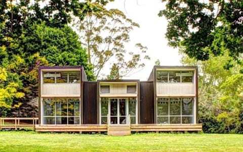 Two-storey dark-clad building with extensive glazing and a timber deck, set in a grassed park