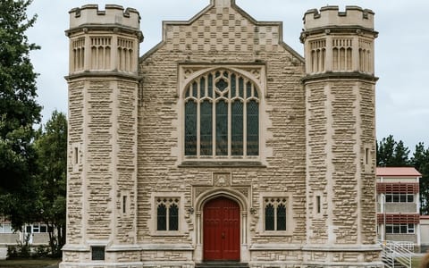 Stone Gothic building with corner turrets, arched windows, and red double doors