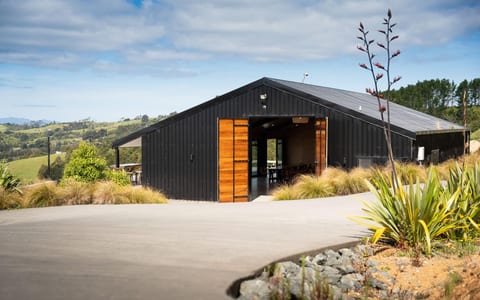 Black board-and-batten barn with timber doors and native planting on a hillside farm