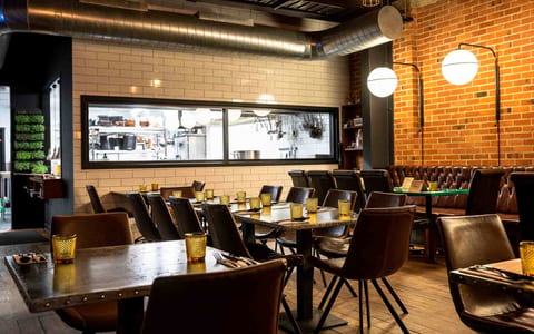 Brick-walled restaurant with dark timber tables, pendant lights, and pass window to kitchen