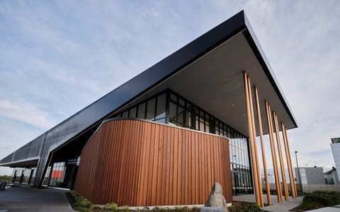 Contemporary building with curved dark timber cladding, metal roof canopy, and tall bronze columns