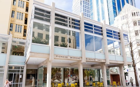 Glass-fronted Pioneer Womens Memorial Hall building on city square with outdoor cafe seating