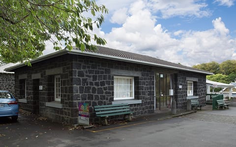 Small dark stone masonry building with bench seating at the entrance