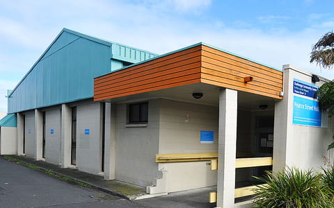 Low community hall exterior with teal metal roof and timber cladding canopy