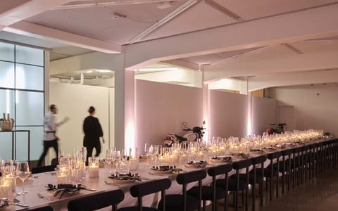 White warehouse interior with long candlelit table, concrete floor, and pink uplighting