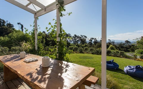 Timber deck with table under white pergola, lawns and garden leading to distant hills view