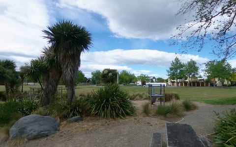 Open park area with native plantings, grass, and small play structure