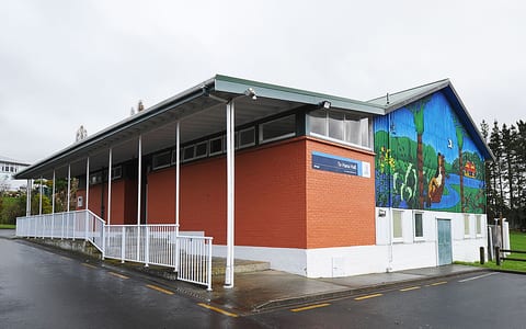 Red brick hall with covered verandah, white railings, and a large painted mural on the gable end