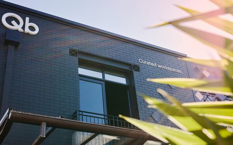 Dark brick building facade with Qb logo and curated workspaces text, viewed from below