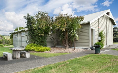 Small weatherboard hall with green gabled roof set in grass with trees behind