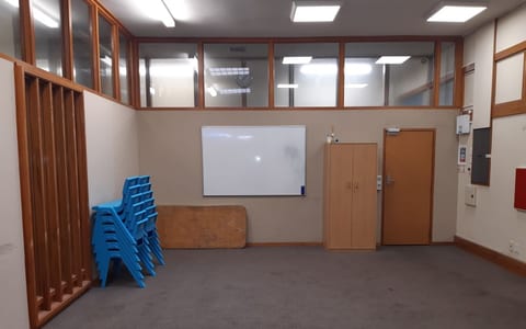 Empty carpeted room with stacked blue chairs, whiteboard and high windows