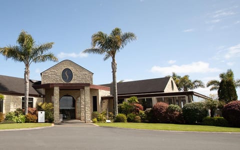 Stone and timber winery building with palm trees and formal driveway