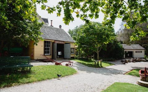 19th-century village buildings amid trees with gravel paths and farm equipment