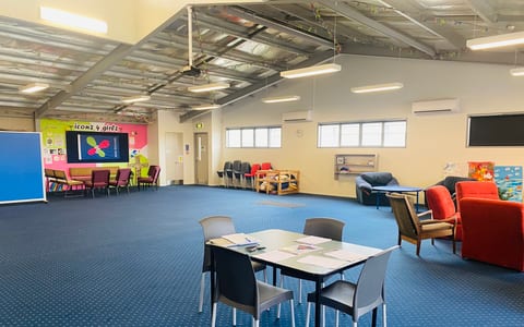 Large open room with blue carpet, tables, chairs, and colourful wall mural