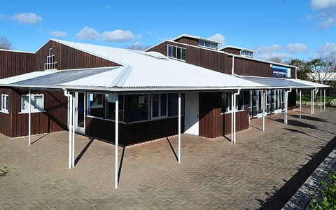 Dark brown community centre building with covered entrance and brick paving