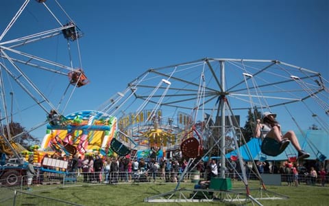 Fairground rides and crowds on open grass at outdoor show event