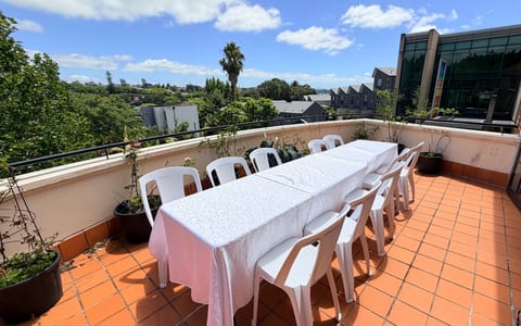 Rooftop terrace with long white-clothed table, white chairs, and city views in background