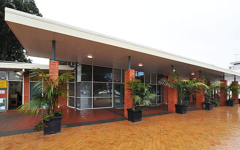 Single-storey brick community centre with covered entrance and potted palms on tiled forecourt