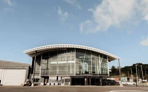 Curved glass and steel waterfront building with helipad markings in foreground