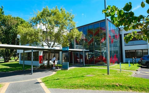 Campus building exterior with glass facade, lawn, and trees under a blue sky