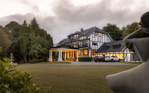 Large Tudor-style manor house with white and dark timber facade set on lawn at dusk