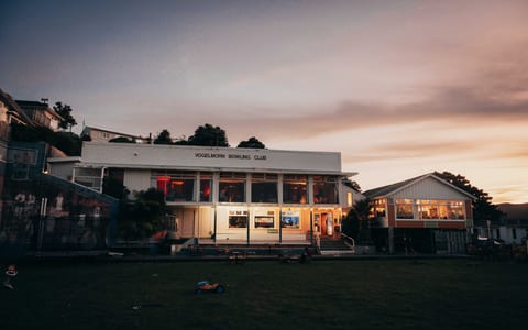 Vogelmorn Bowling Club building lit up at dusk with green lawn in foreground