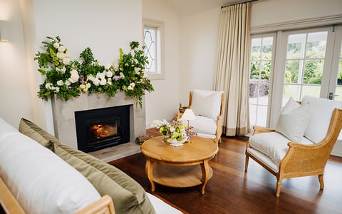Homestead sitting room with fireplace, floral mantle arrangement, and cane armchairs