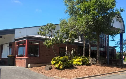 Community hub building with brick and metal cladding, trees, and garden border