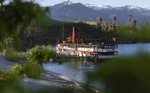 Vintage steamship moored at a timber wharf with trees and snow-capped mountains beyond