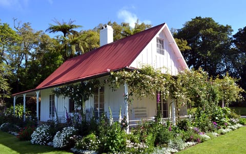 White cottage with red roof surrounded by cottage garden in full bloom